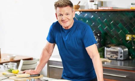 Gordon Ramsay prime rib recipe - Gordon cooking in a kitchen, smiling at the camera with cooking utensils and ingredients around him.